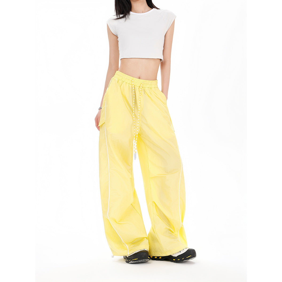 Model wearing bright yellow wide-leg pants with a drawstring waist, pockets, and white side piping.