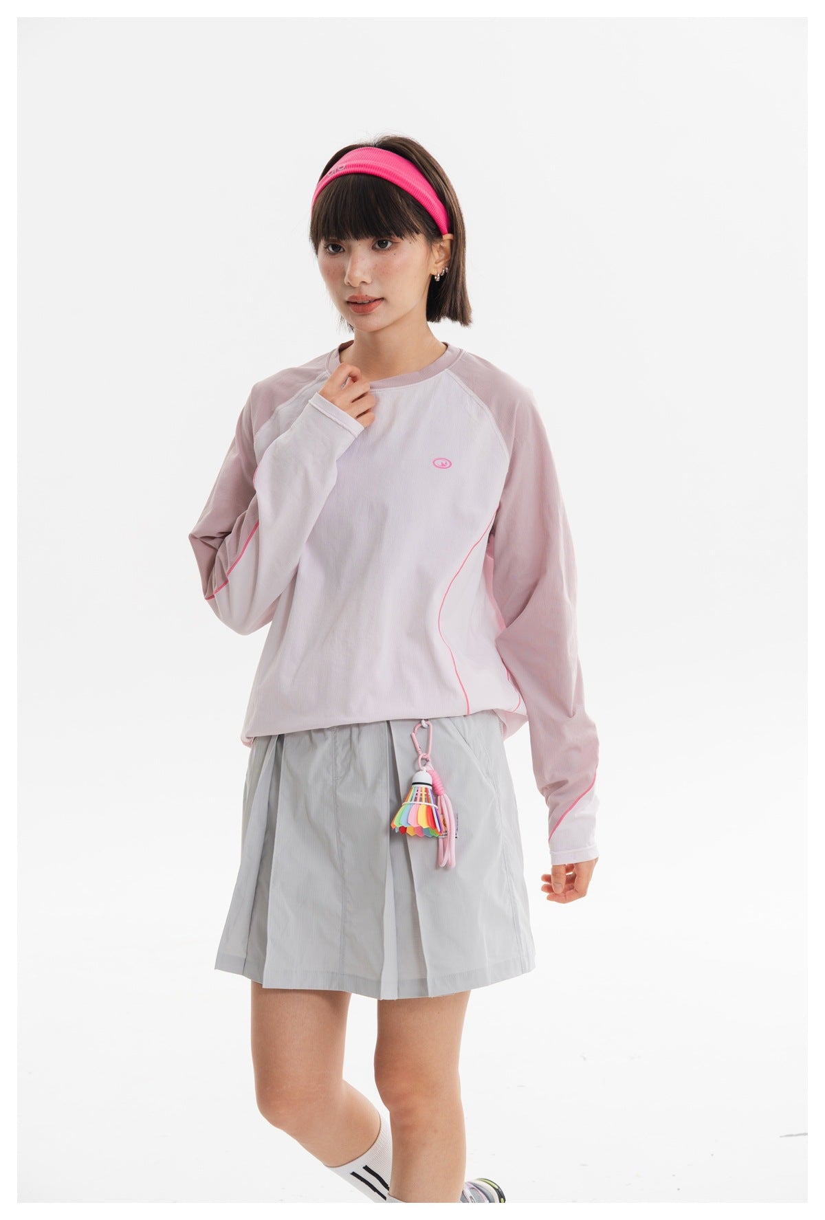 Closer view of a model wearing a pale pink and white long-sleeve top and light gray pleated skirt.