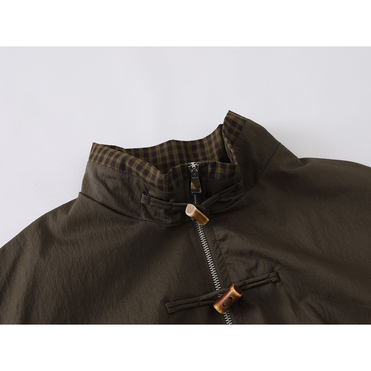 Close-up of a dark olive-brown jacket with a plaid-lined stand collar, metal zipper, and toggle closures.