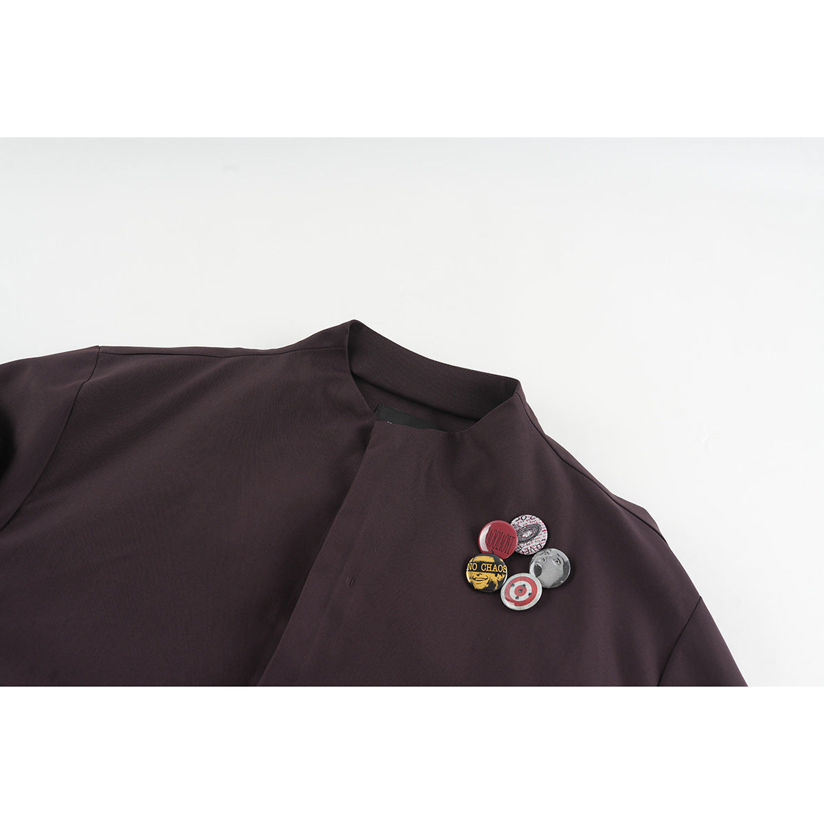 Close-up of a dark plum jacket neckline and chest with five colorful decorative pins.