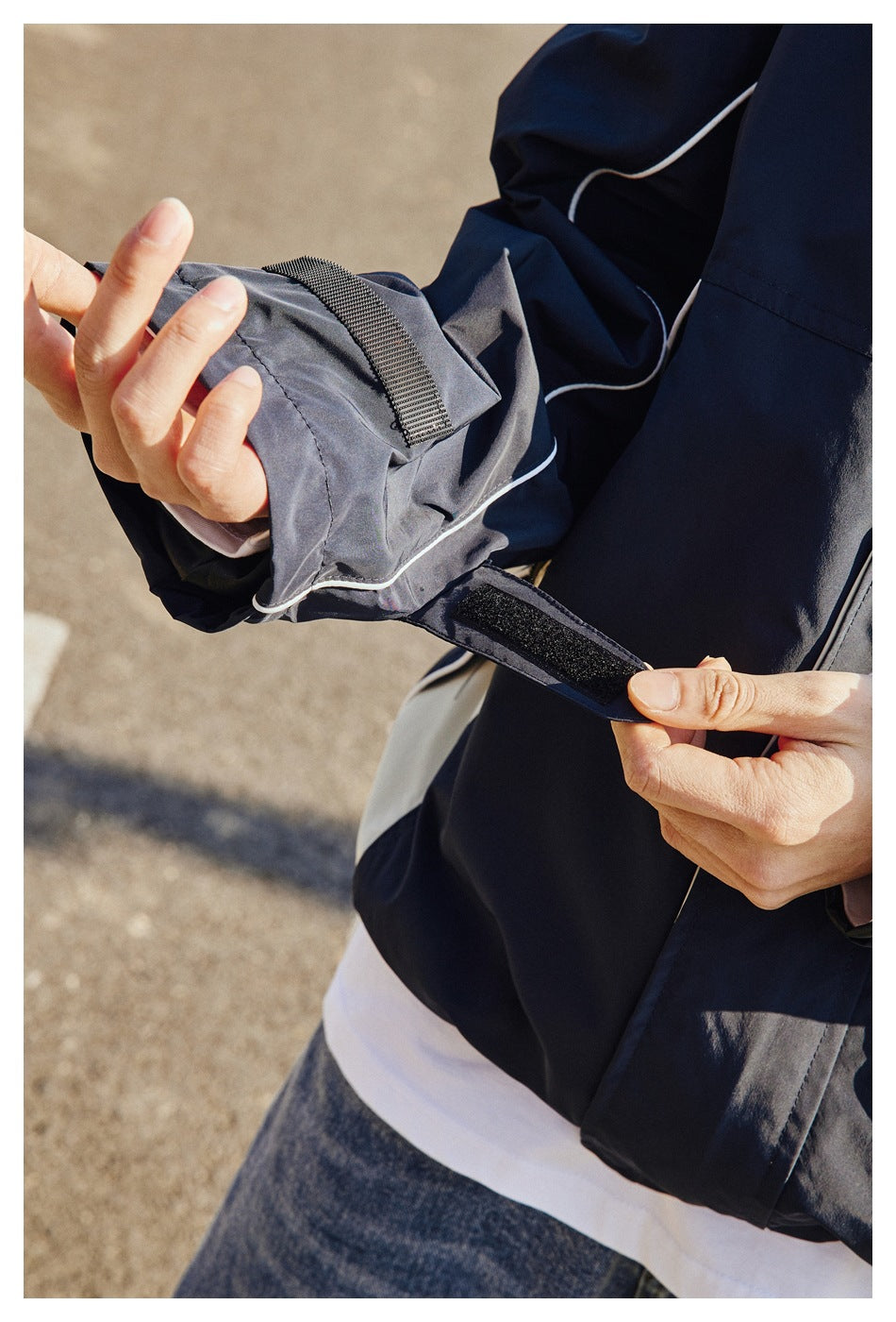 Close-up of the navy jacket's sleeve cuff, showing adjustable hook-and-loop tabs and white piping.
