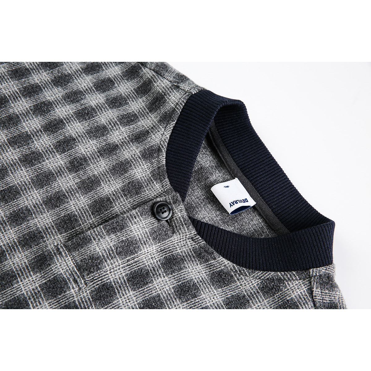 Close-up of a gray plaid jacket neckline with navy ribbed trim, a black button, and a white neck label.