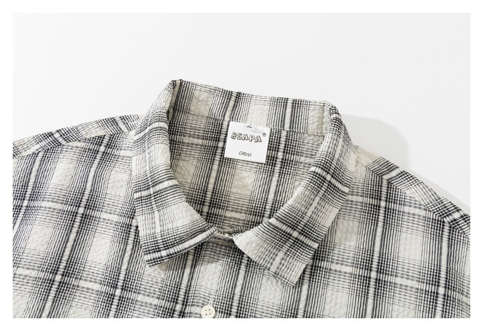 Close-up of a cream and black plaid shirt collar, button, and neck label.