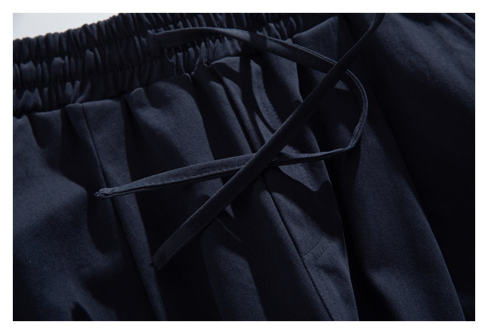 Close-up of dark navy bottoms with an elastic waistband, drawstring, pleats and pocket seam.