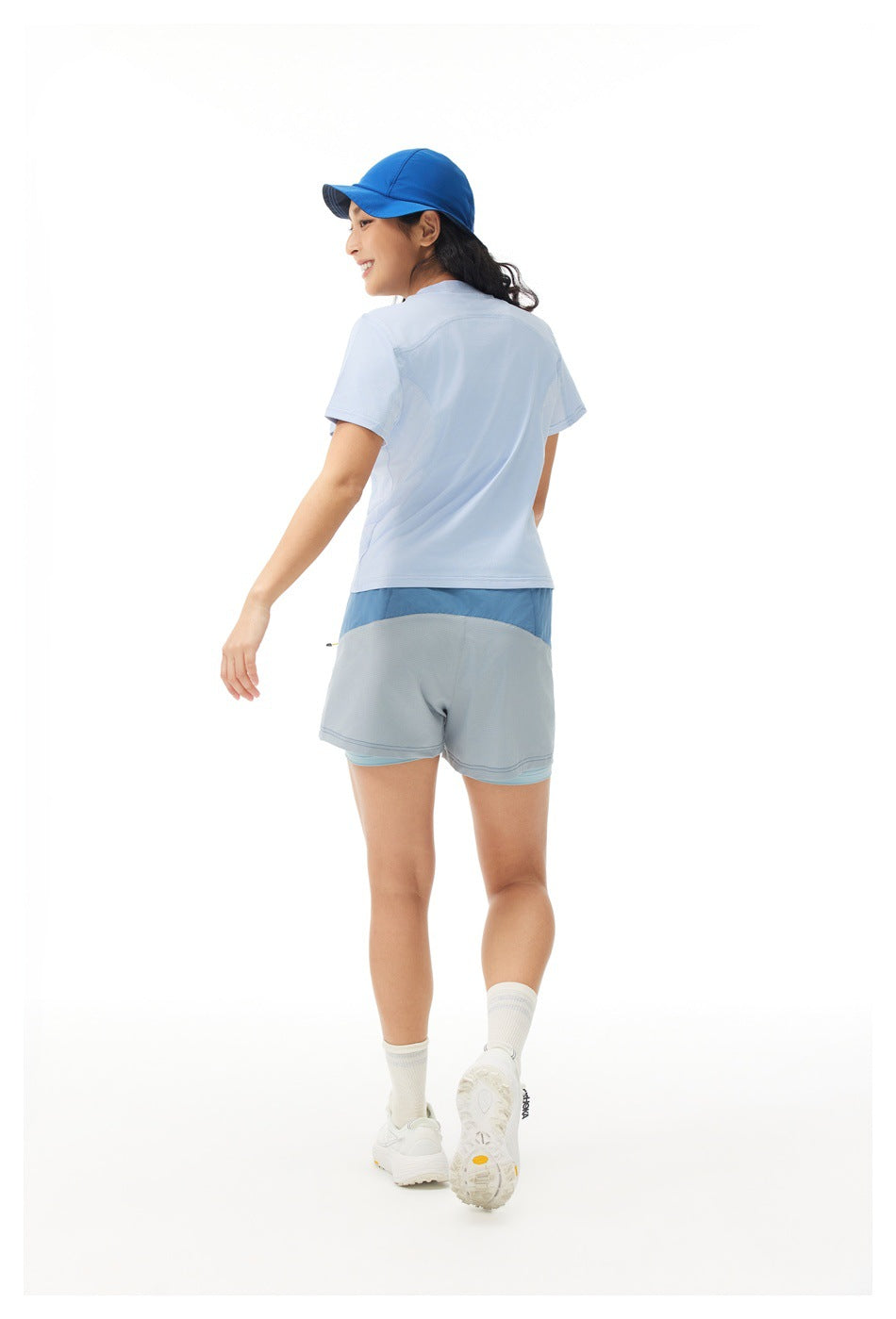 Rear view of a woman wearing a pale blue short-sleeve shirt and blue-gray color-block shorts.