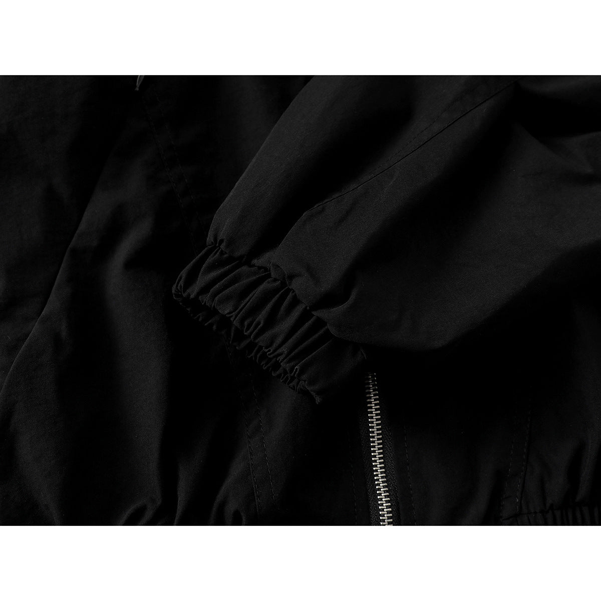 Close-up of a black jacket sleeve with an elasticated cuff beside the front zipper.