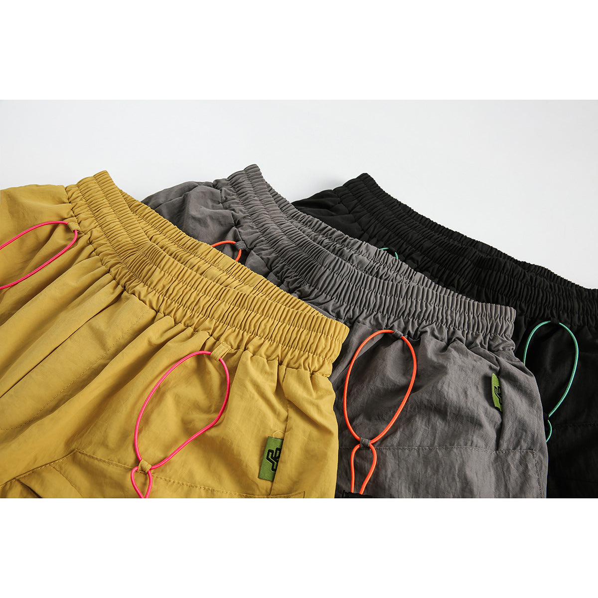 Close view of mustard, gray, and black shorts with elastic waists and contrasting cord details.