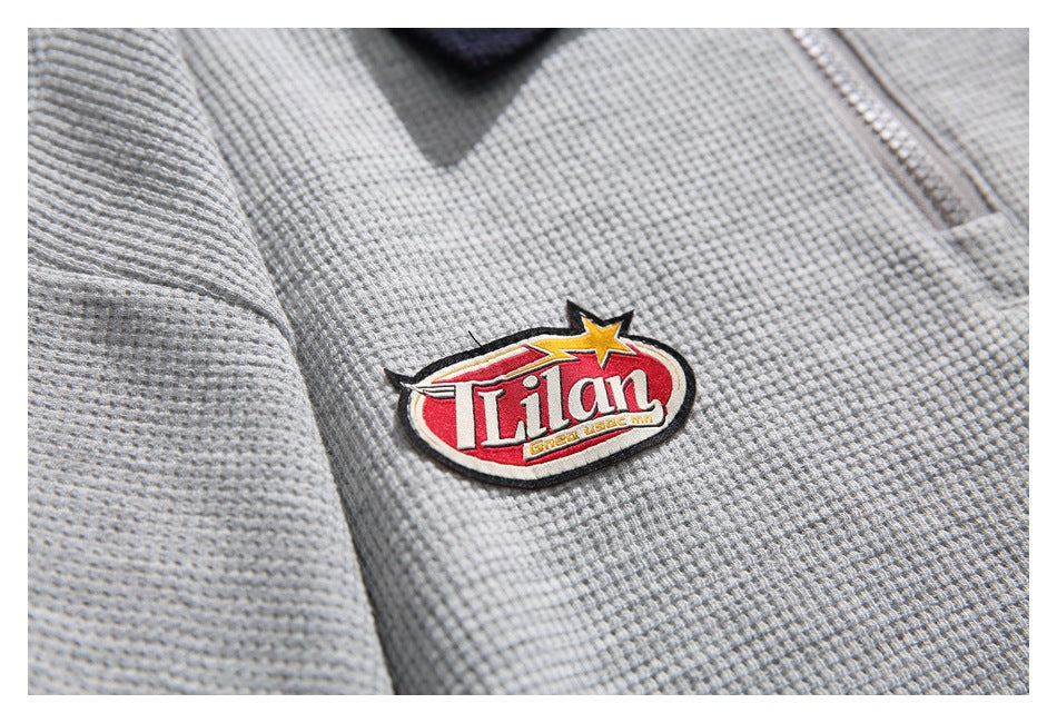 Close-up of a red, white, and yellow embroidered patch on the gray textured pullover.