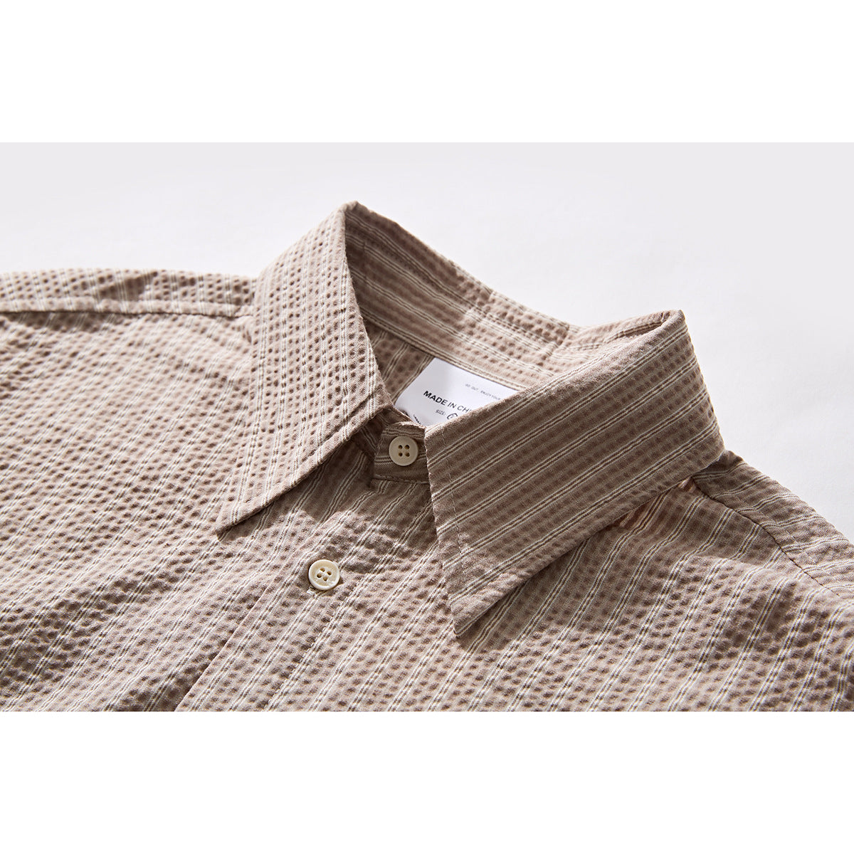 Close-up of a beige-brown textured button-up shirt collar, upper placket, and cream buttons.
