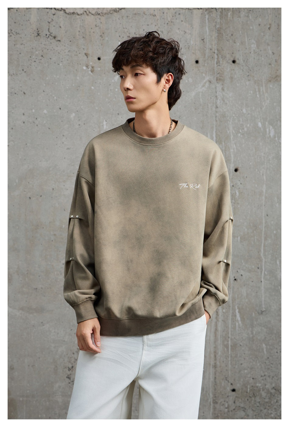 Front view of a model in a taupe oversized sweatshirt with white chest script and metal sleeve studs.