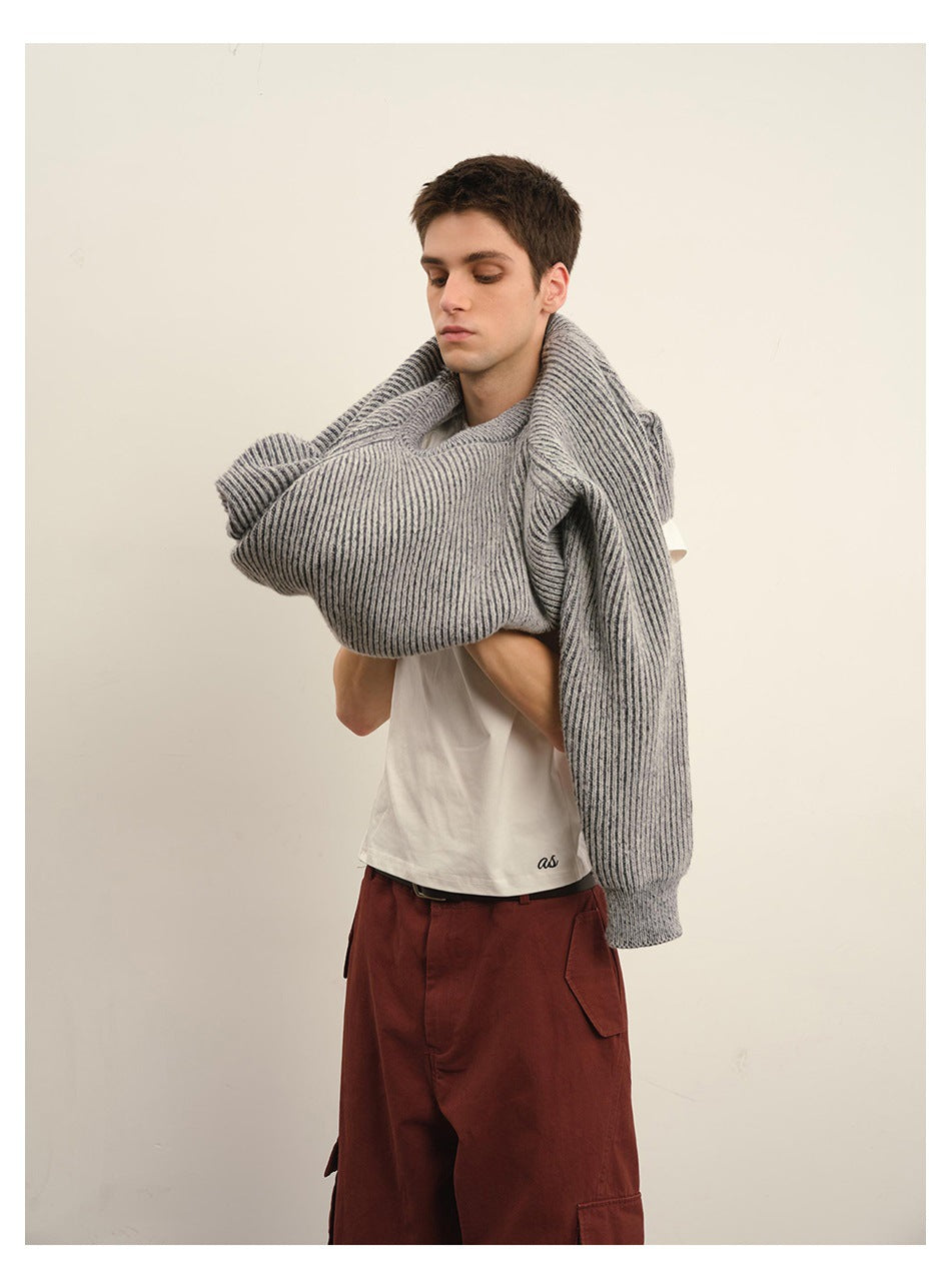 Male model holding a gray ribbed sweater across his shoulders, revealing a white T-shirt and rust-red cargo pants.