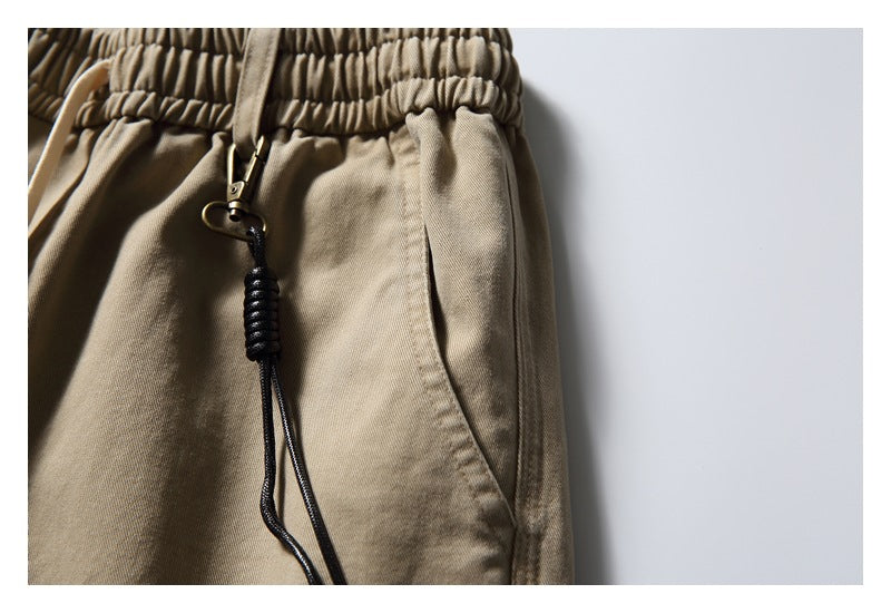Close-up of khaki trousers showing the elastic waistband, pocket opening and black cord attachment.