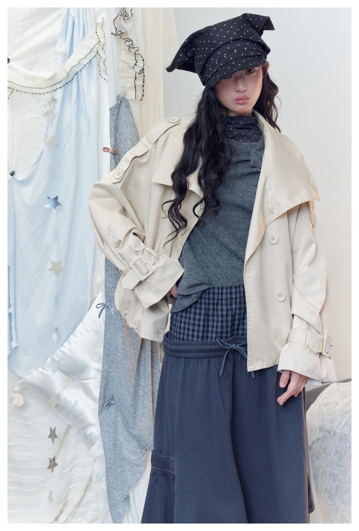 Model wearing an oversized cream jacket with wide lapels and cuff straps, styled over a gray top and navy bottoms.