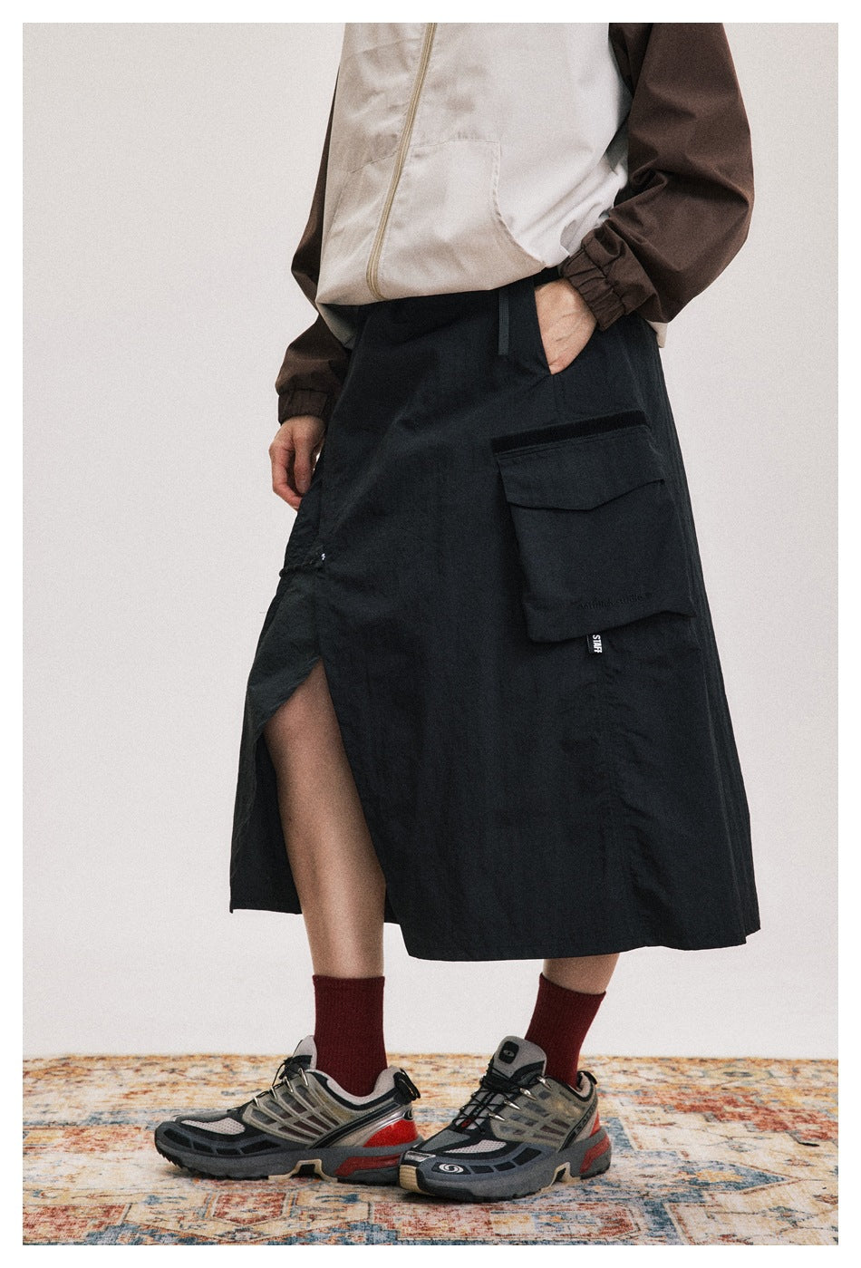 Person wearing a black midi cargo skirt with a front slit and large flap pocket, styled with red socks and sneakers