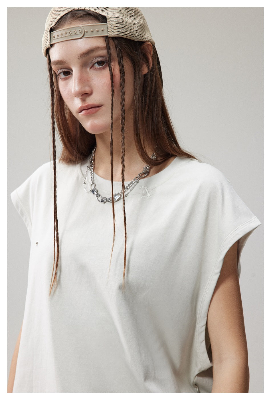Close view of a model wearing a white sleeveless top with a small embroidered chest emblem.