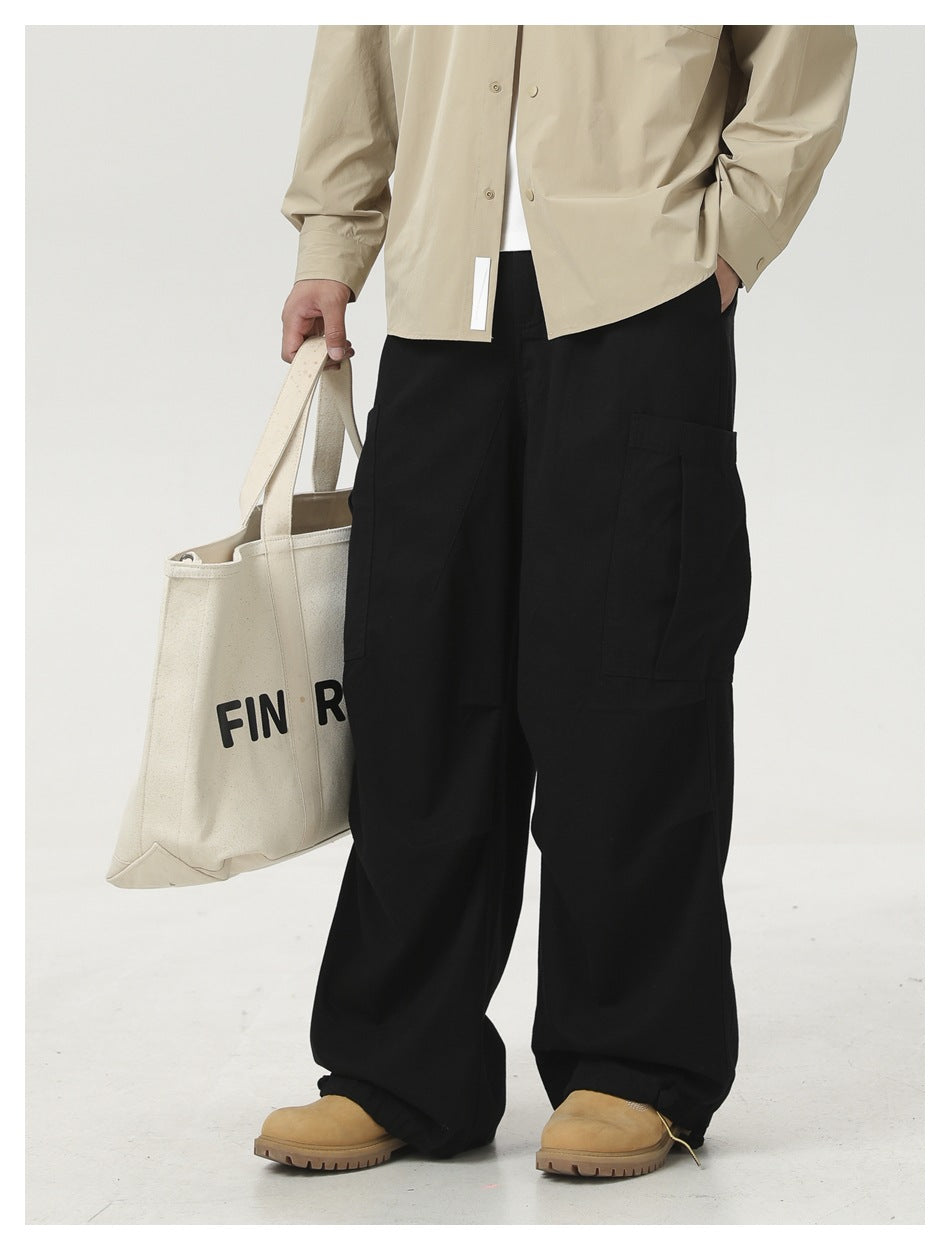 Cropped outfit view of a model in a light beige shirt and black cargo pants, carrying a printed cream tote.