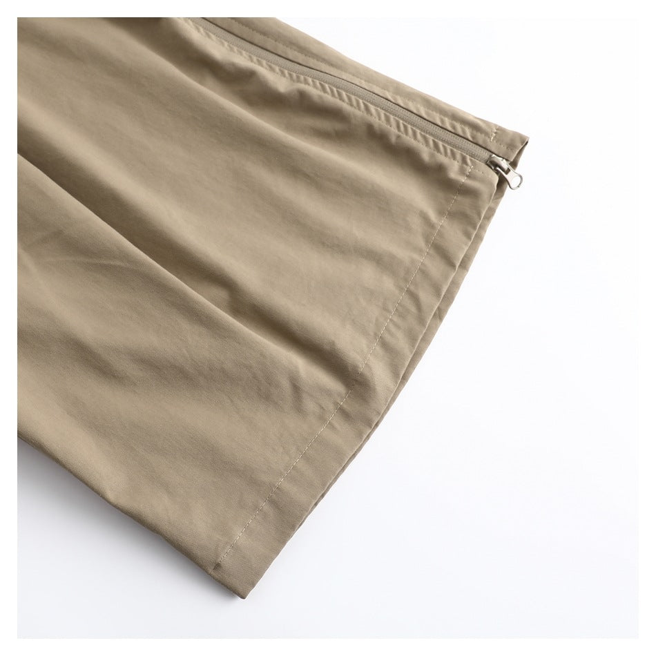 Close-up of a taupe trouser leg with a long zipper near the hem.