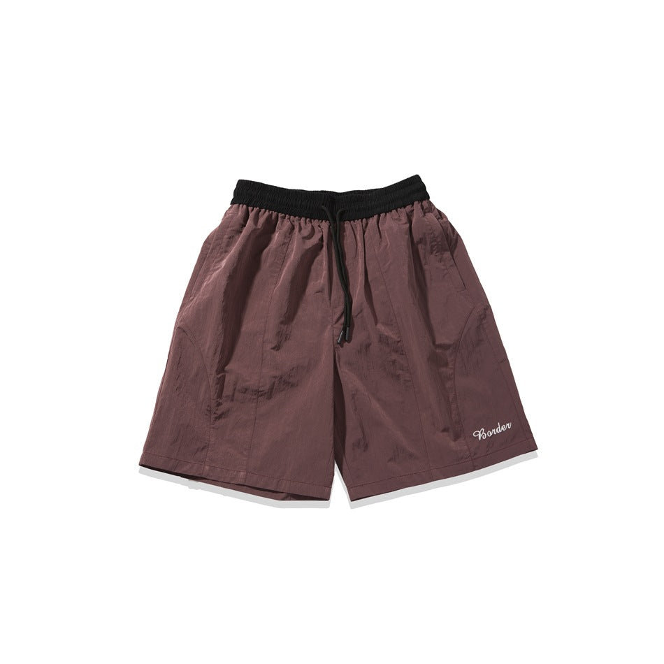 Burgundy-brown knee-length shorts with black elastic waistband, drawstring and white script embroidery, flat lay