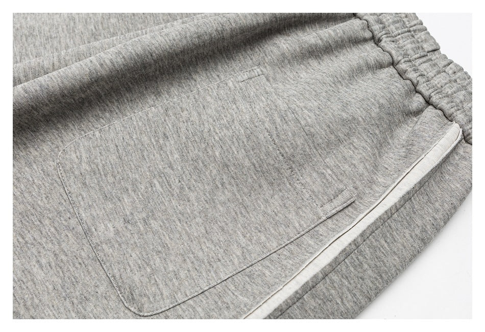 Close-up of a large stitched patch pocket on gray heathered pants, beside light-colored trim.