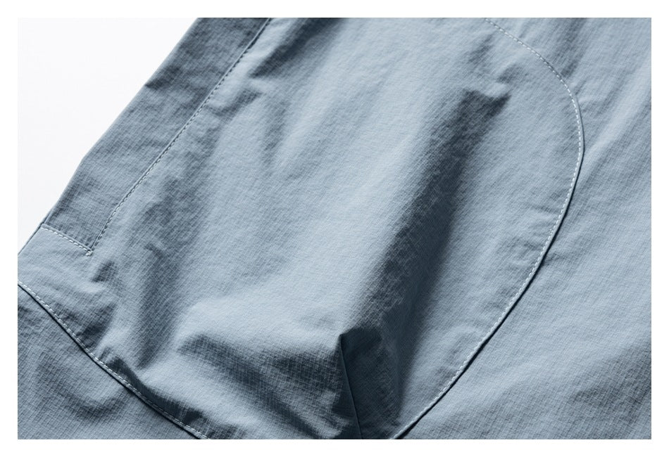 Close-up of a curved patch pocket and stitching on light blue fabric.