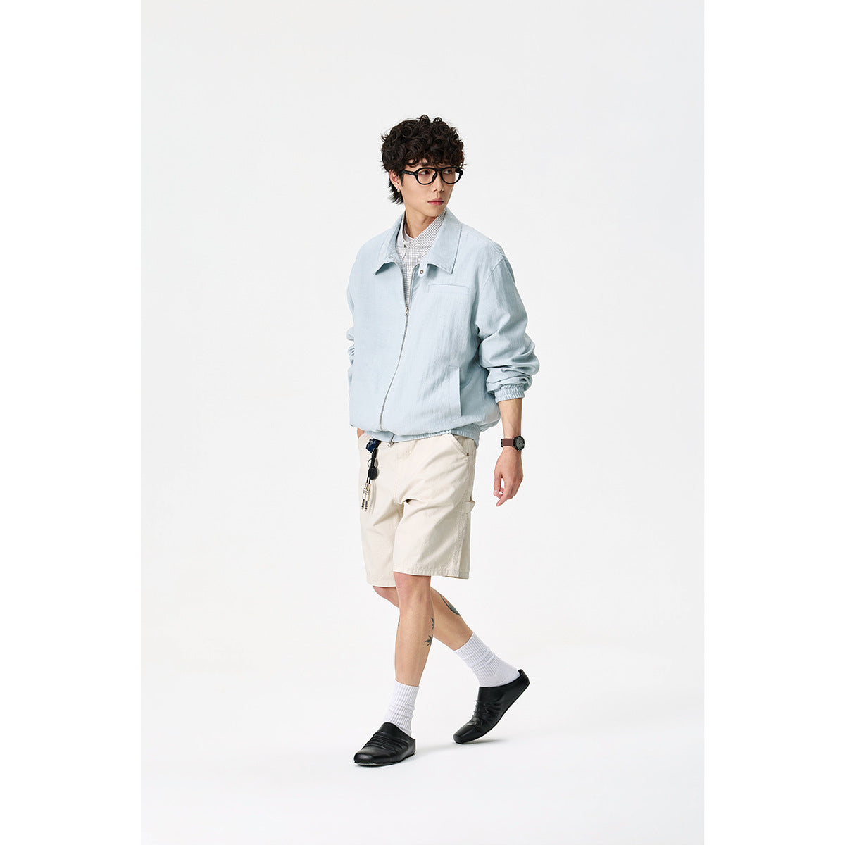 Model walking in a pale blue zip-front jacket with cream shorts, shown from a three-quarter angle.
