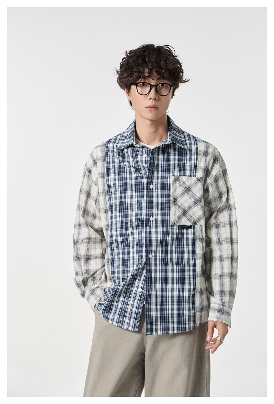 Front view of a model wearing a buttoned navy, gray and white patchwork plaid shirt with a chest pocket.