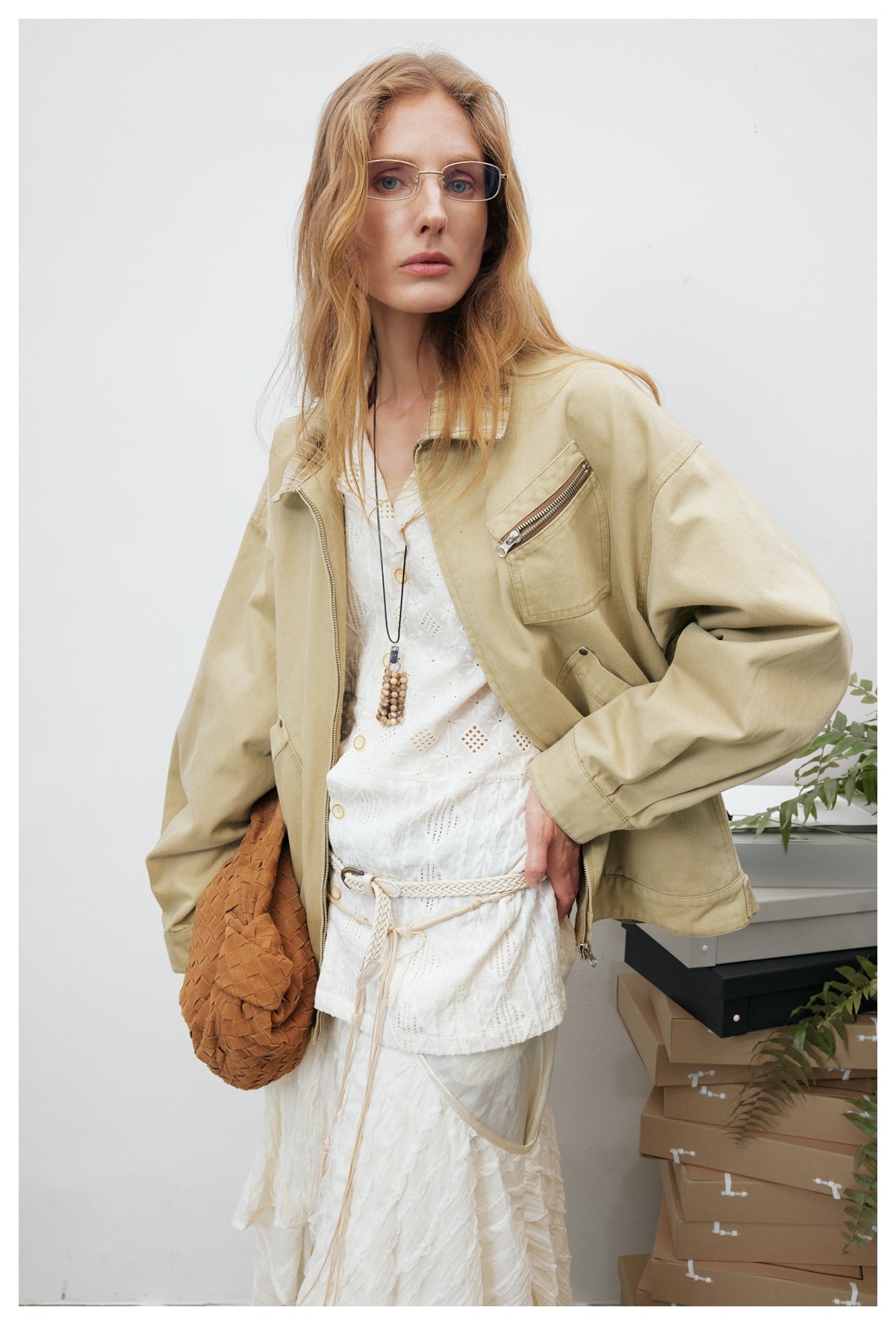 Close view of a model wearing a beige jacket with a plaid collar and zip chest pocket over white clothing.