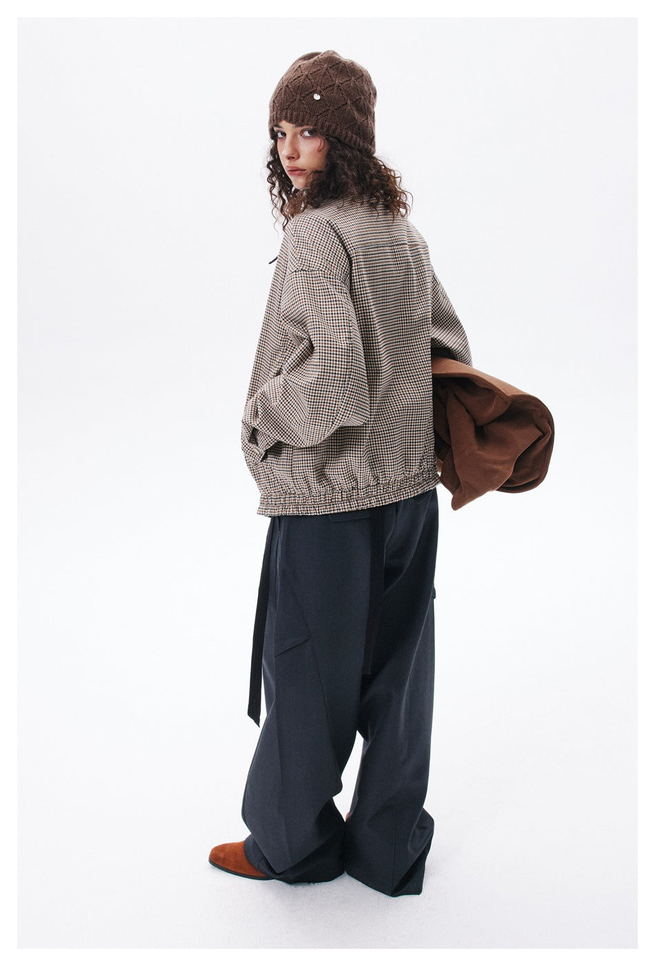 Rear view of a model wearing a beige-and-brown check jacket and navy wide-leg trousers with a brown knit beanie.