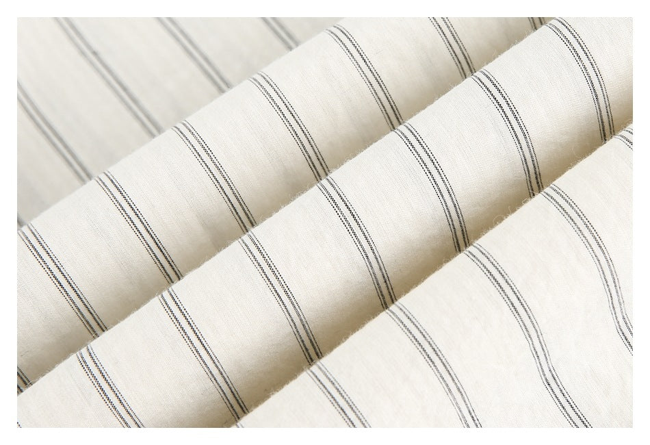 Close-up of cream fabric folded into ridges, showing fine dark vertical stripe patterns.