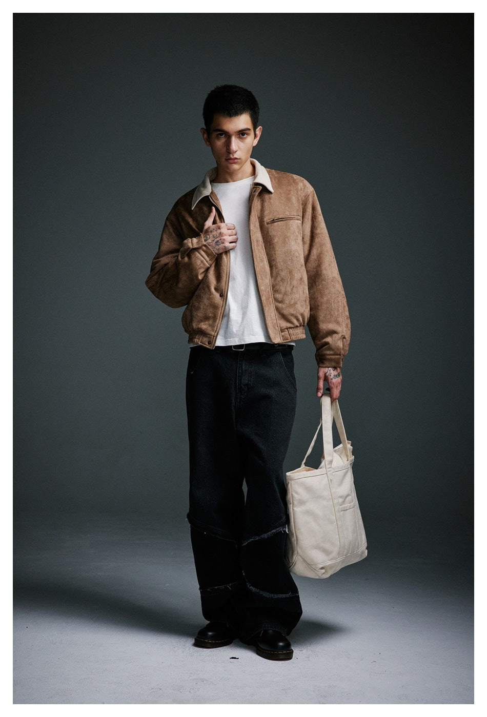 Model wearing khaki suede-look jacket open over a white tee with black wide-leg jeans, holding a cream tote bag