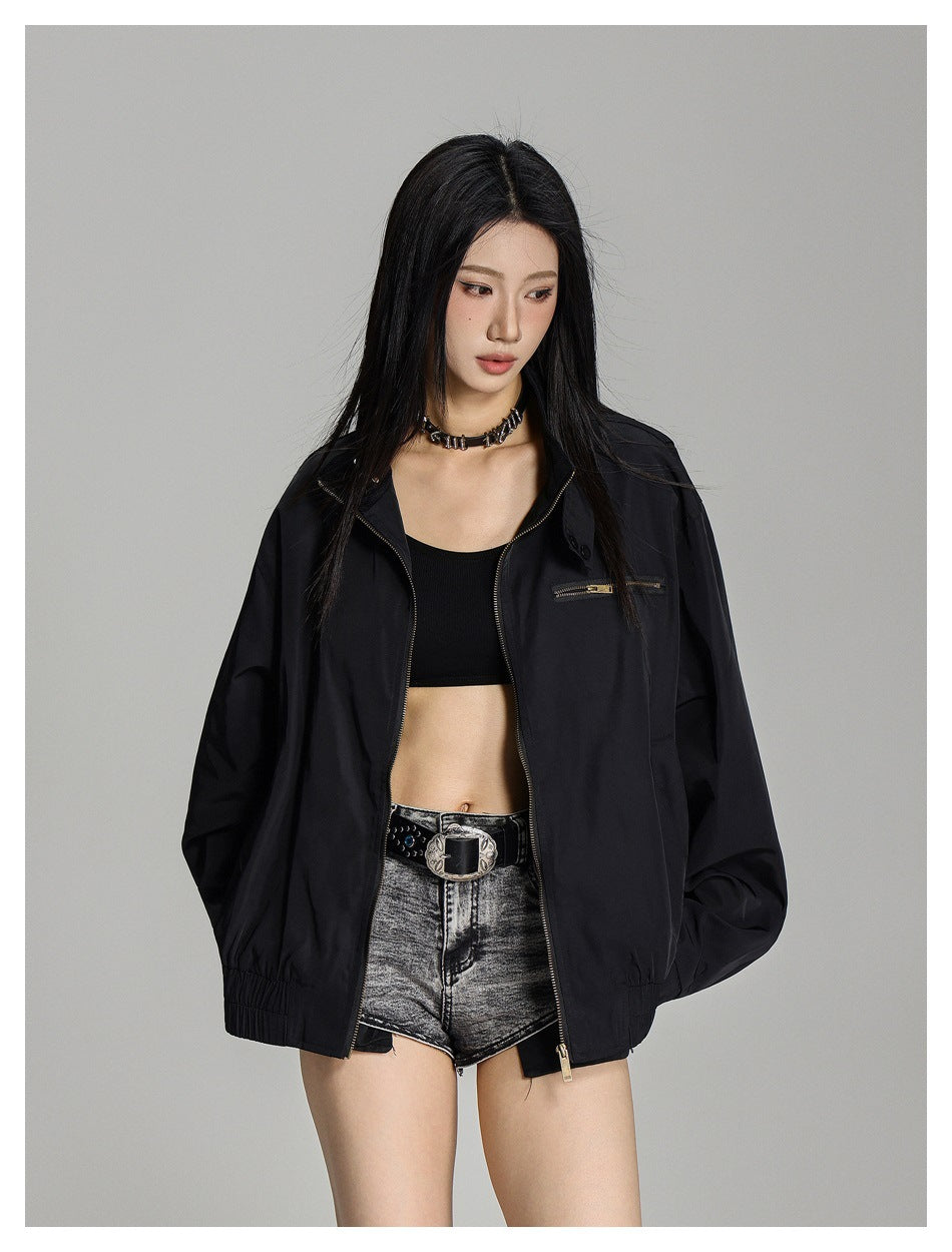 Model wearing an open black jacket with a chest zip pocket over a black crop top and gray denim shorts.