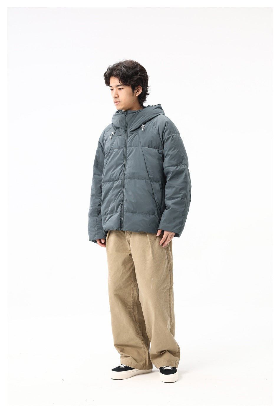 Man wearing a blue-gray hooded puffer jacket with khaki wide-leg pants and dark sneakers