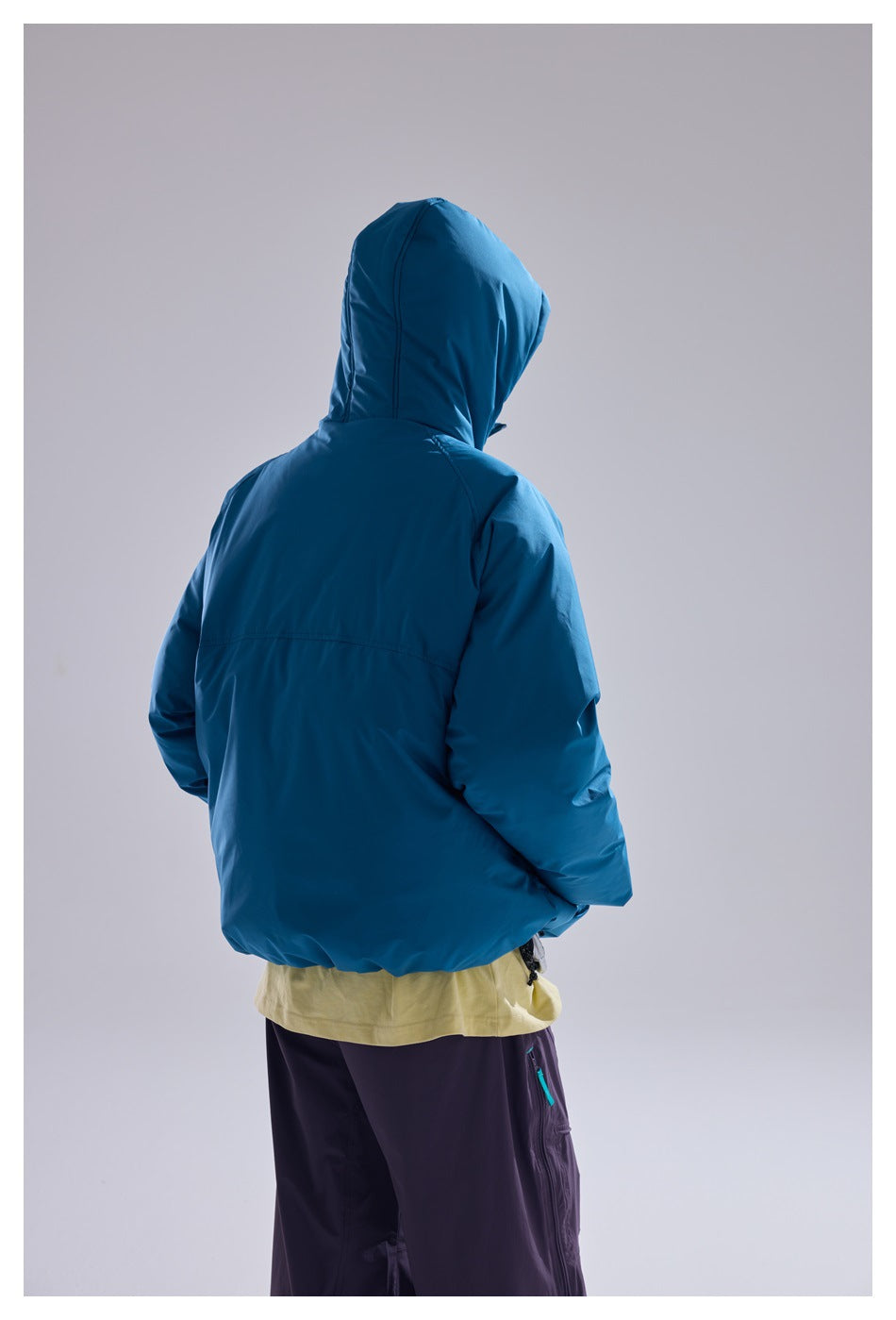 Back view of a person wearing a blue hooded padded jacket with a yellow top and dark purple pants