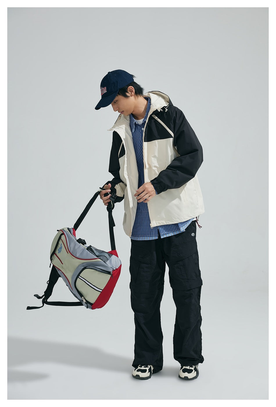 Full-length model wearing a black-and-cream hooded jacket with black cargo pants and carrying a bag.