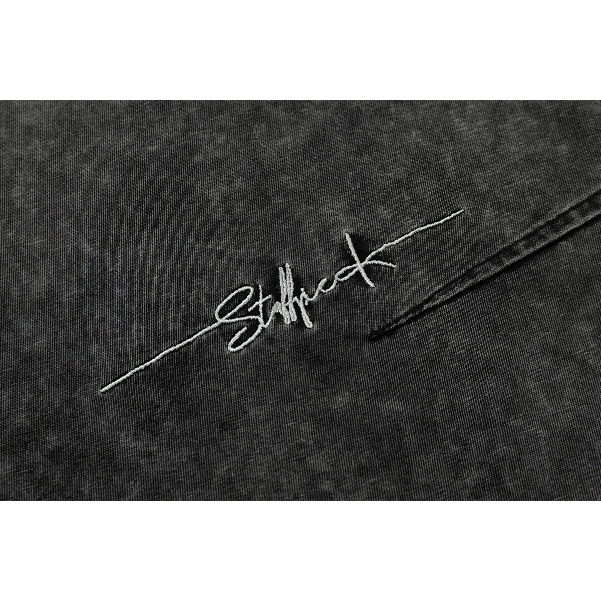 Close-up of white cursive embroidery on black acid-wash T-shirt fabric.