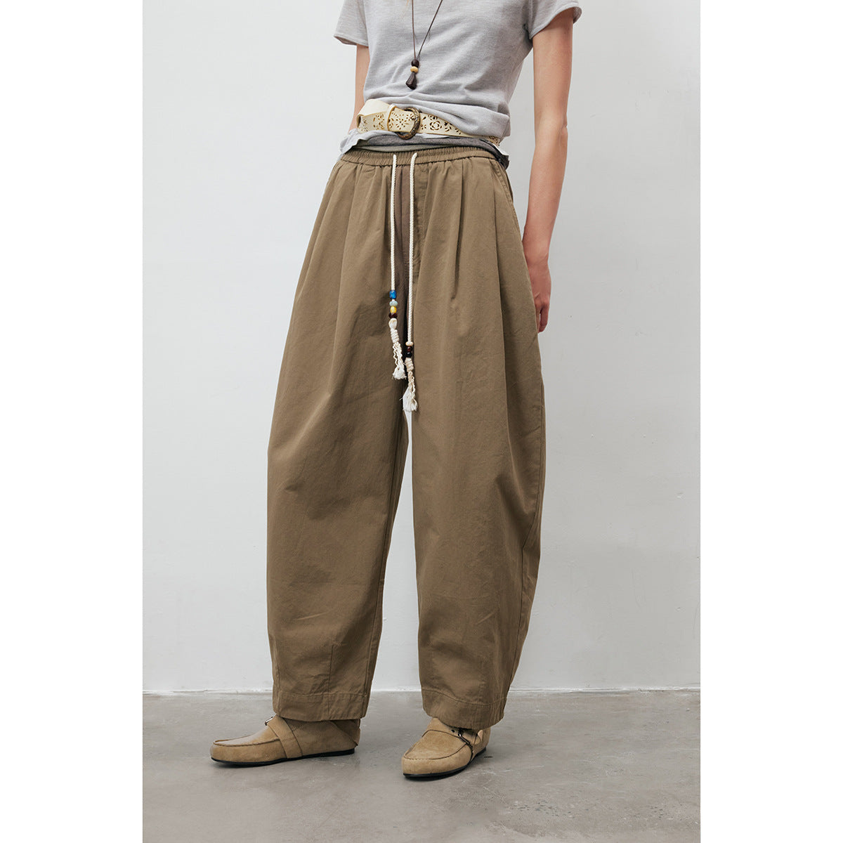 Model wearing loose taupe drawstring trousers with beaded tassels and loafers.