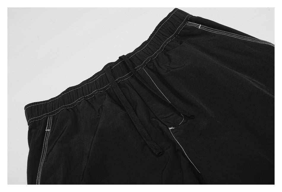 Angled close-up of the black pants' elastic waistband, drawstring, pocket opening, and light contrast stitching.
