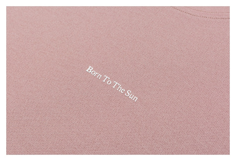 Close-up of white “Born To The Sun” lettering on dusty rose perforated fabric.