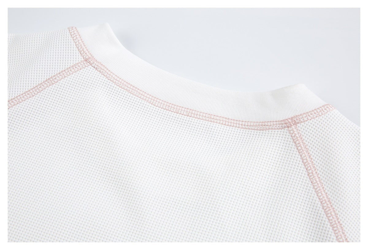 Close-up of a white ribbed neckline with pale pink stitching along the collar and shoulder seams.