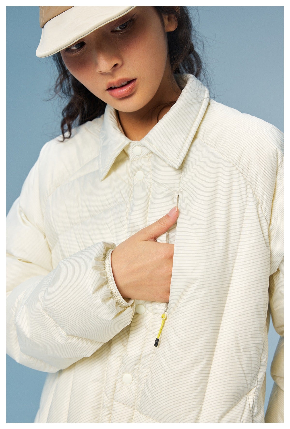 Close-up of an ivory jacket showing its fine pinstripes, pointed collar, snap placket, and chest pocket.