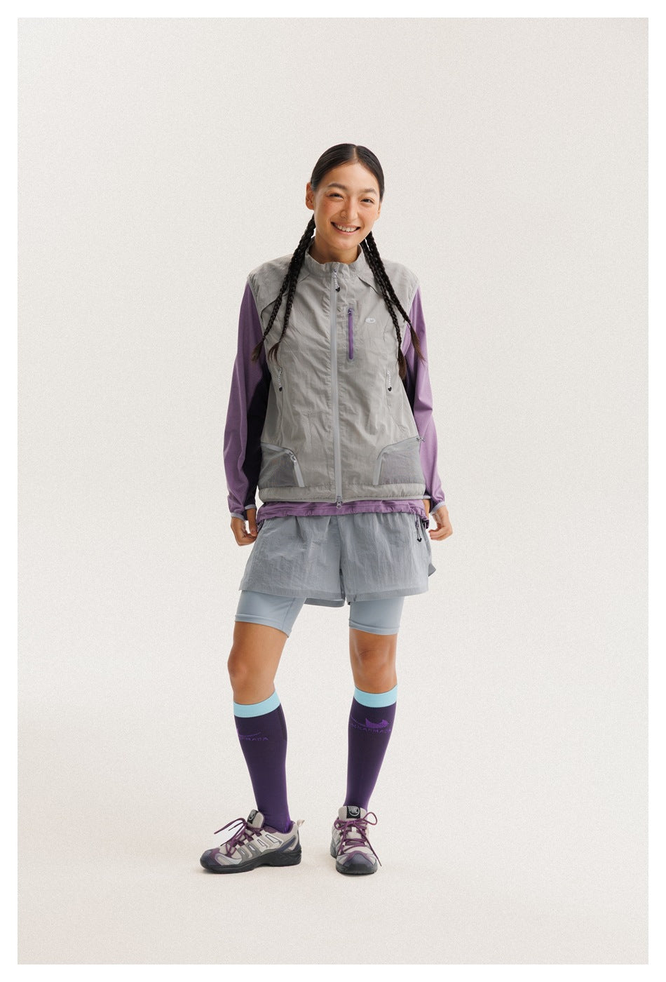 Full-length front view of a model in a gray vest over a purple top, gray shorts, and purple knee-high socks.