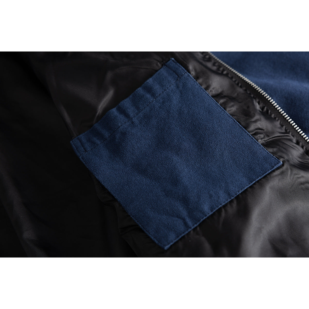 Close-up of a navy jacket's rectangular outer pocket against black lining, with part of the silver zipper visible.