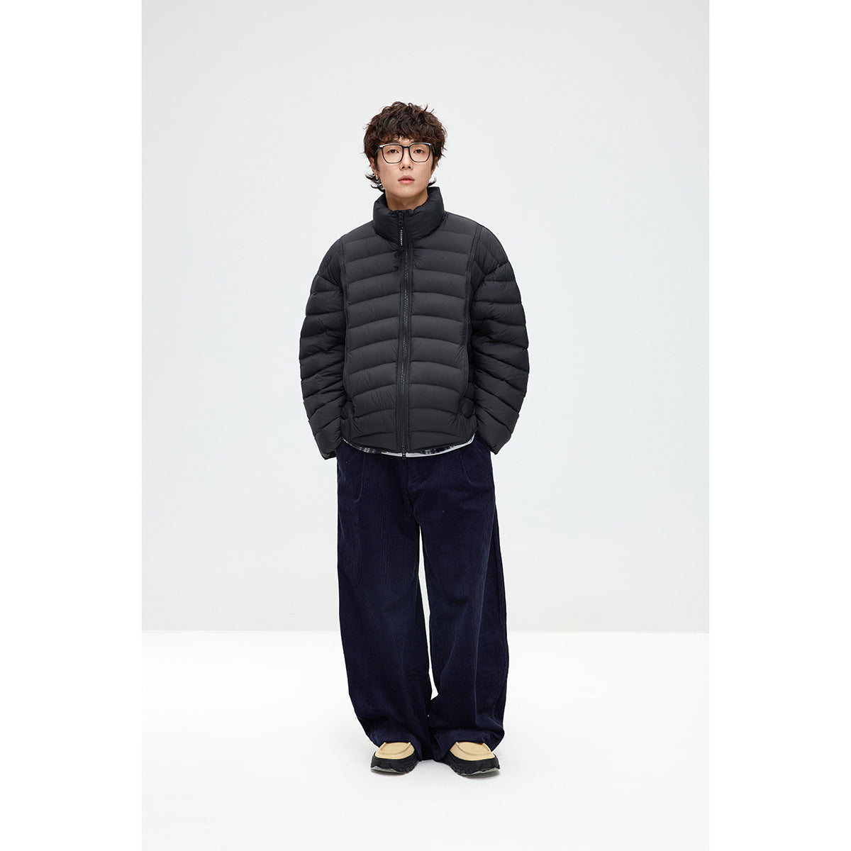 Model wearing a black horizontally quilted puffer jacket with a high collar, zipped over dark wide-leg trousers.