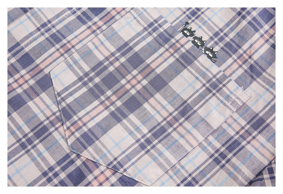 Close-up of the plaid shirt's chest pocket and small black cat motif on pale blue-gray and blush checks.