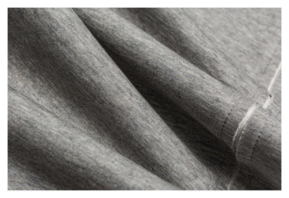 Macro view of gray heathered pant fabric, folds, stitching, and a narrow light-colored edge trim.