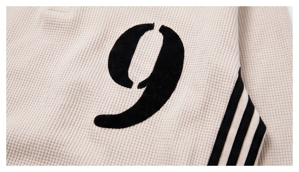 Close-up of a cream waffle-knit garment with a bold black curved graphic and three black sleeve stripes.