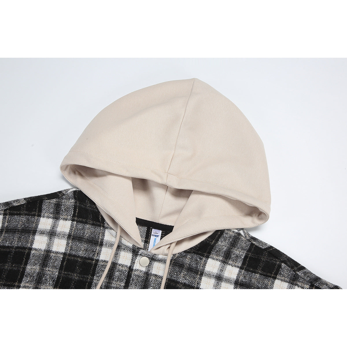 Close-up of a beige hood and drawstrings on a black, gray, and white plaid hooded overshirt.