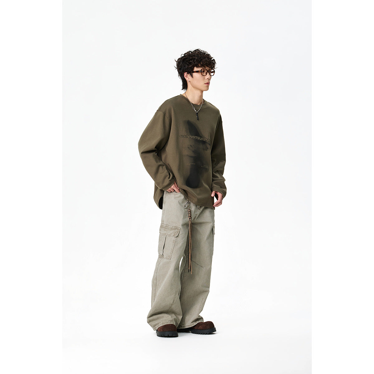 Model wearing an olive long-sleeve graphic shirt and loose light-gray cargo pants; three-quarter view.