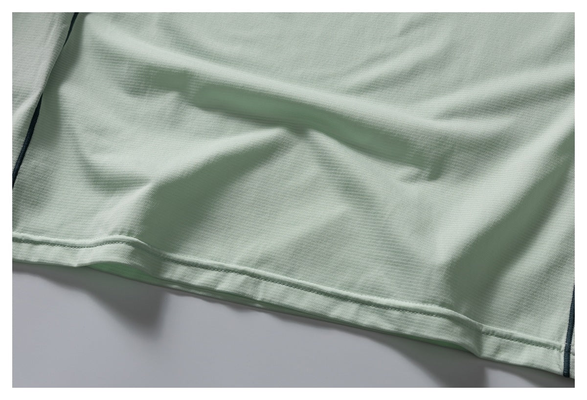 Close-up of the pale mint-green garment's stitched bottom hem and dark piping at the sides.