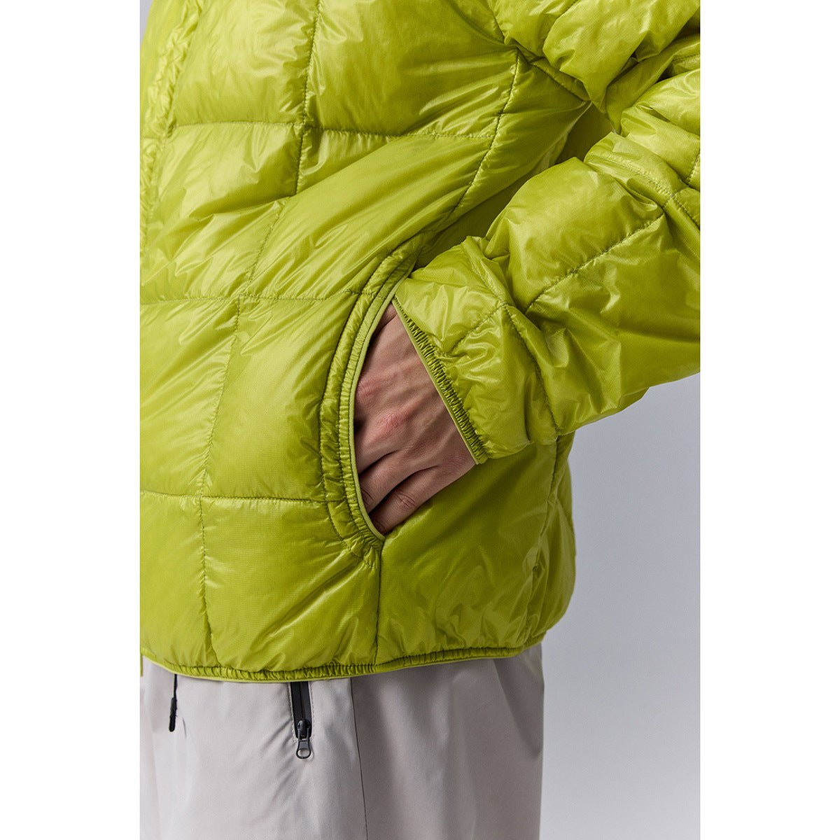 Close-up of a lime-green quilted jacket showing its elastic-trimmed pocket and hem.